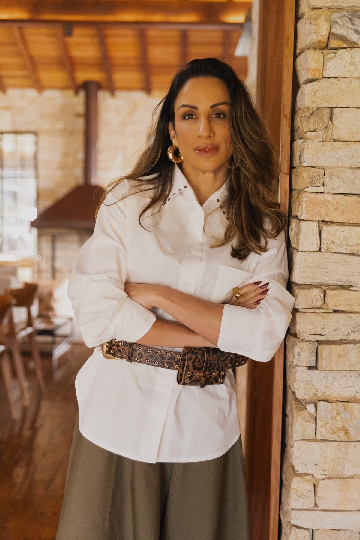 Deb Torrez, de camisa branca, encostada numa parede de pedra